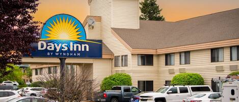 Un Days Inn by Wyndham con un estacionamiento lleno de coches, un edificio de techo inclinado y un cielo despejado.