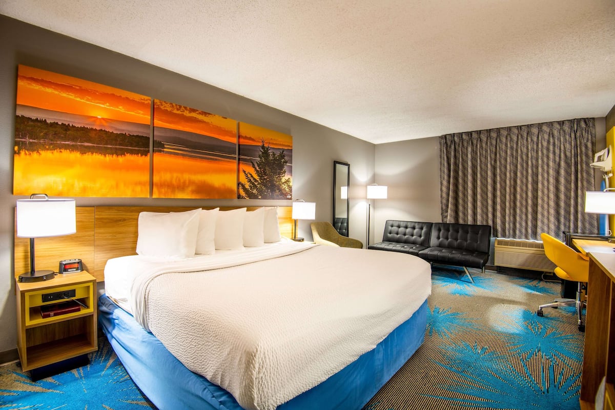 A hotel room with a large bed, a desk with a chair, a sofa, and a large painting on the wall.