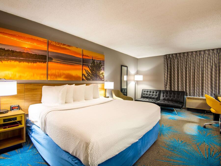 A hotel room with a large bed, a desk with a chair, a sofa, and a large painting on the wall.