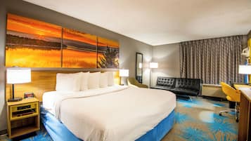 Habitación de hotel con una cama grande, un escritorio, una silla y un cuadro de un atardecer sobre un lago.