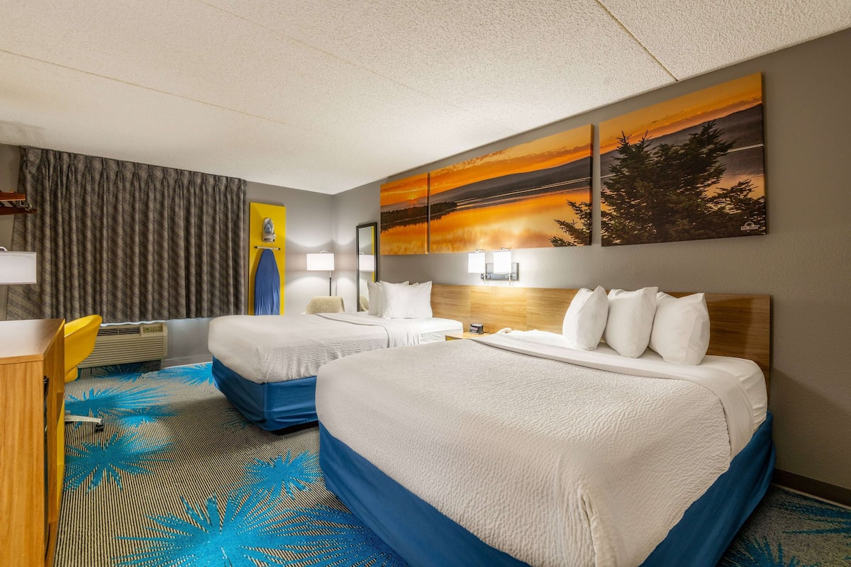A hotel room with two beds, a desk, and a large window with curtains.