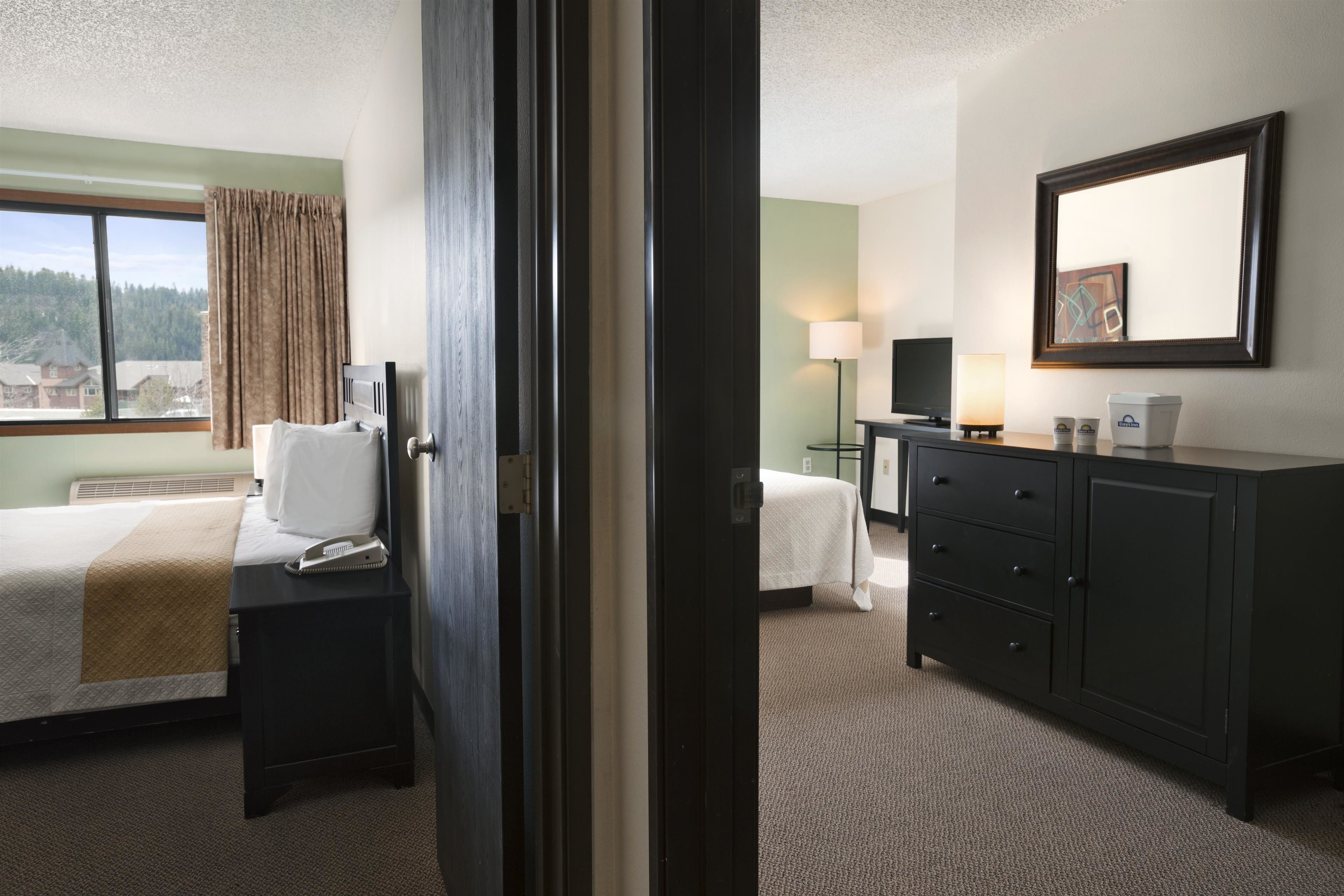 A hotel room with a bed, a desk, a dresser, a lamp, and a window with curtains.