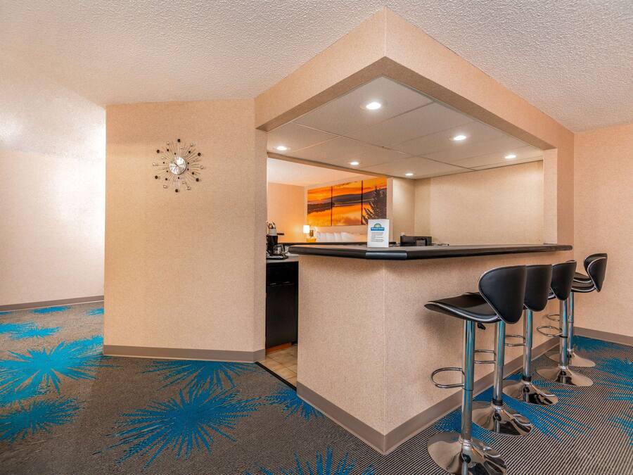 A hotel lobby with a reception desk, three bar stools, a clock, and a painting on the wall.