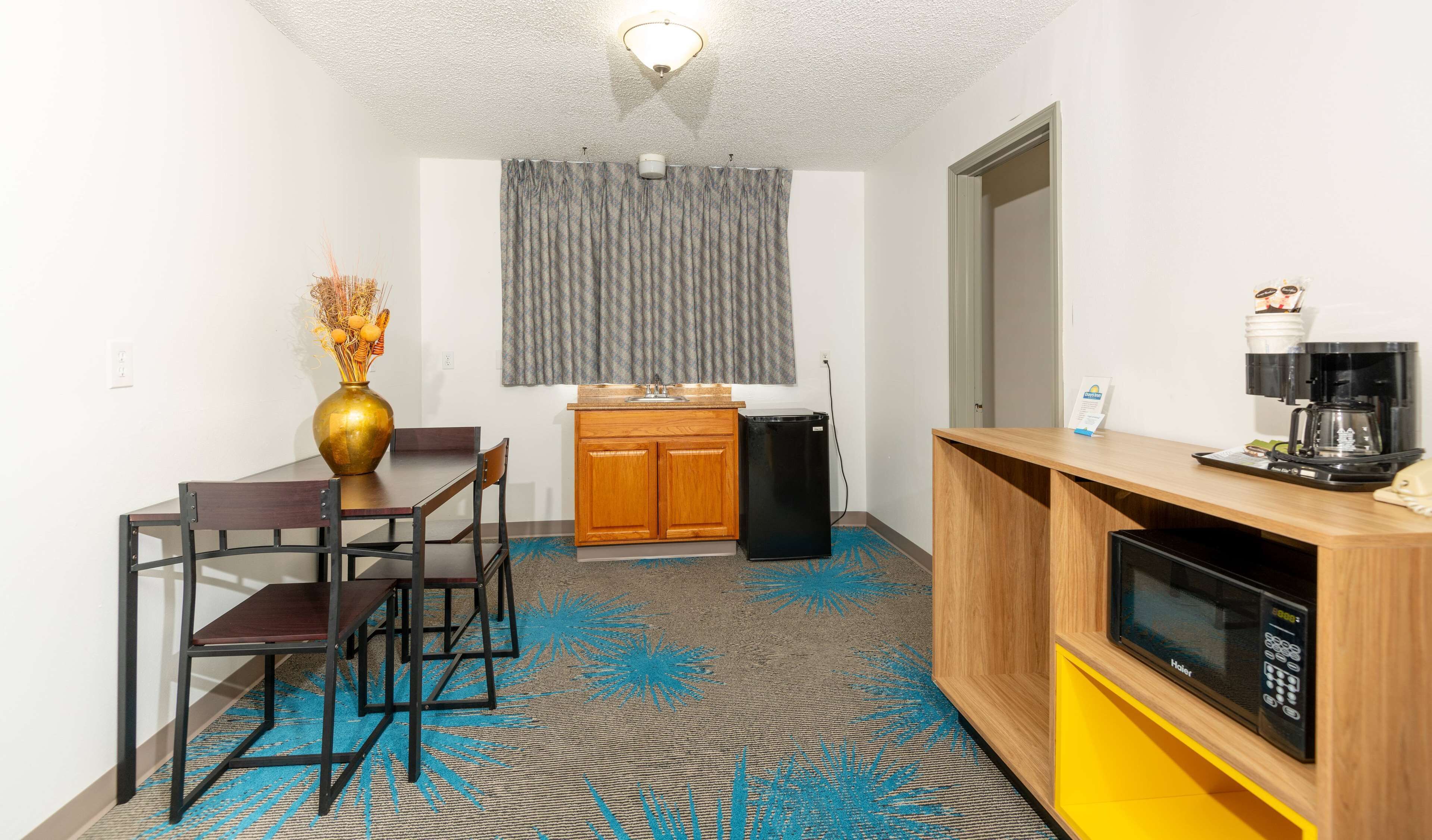 Una habitación de hotel compacta con kitchenette, un comedor con mesa y sillas, un refrigerador pequeño, un microondas y una cafetera.