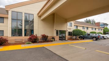 A hotel with a covered entrance, large windows, and a parking area with yellow lines.