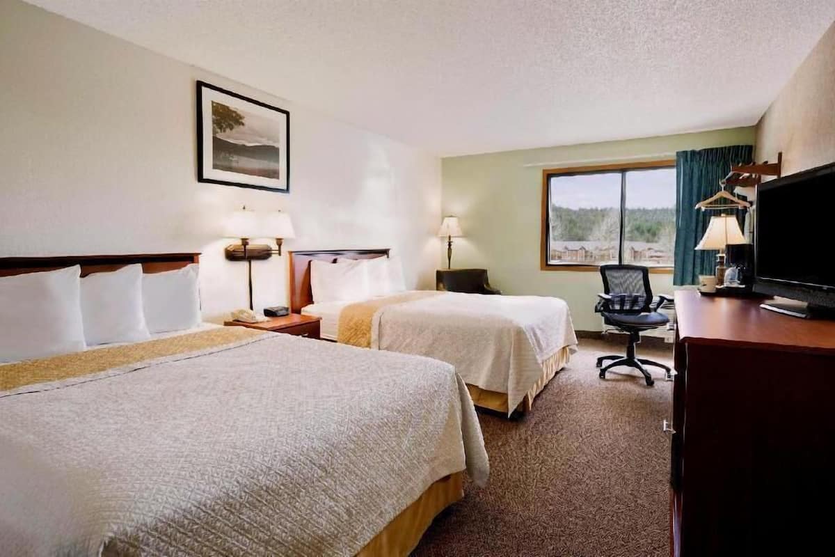 A hotel room with two beds, a desk, a chair, a television, and a window with a view.