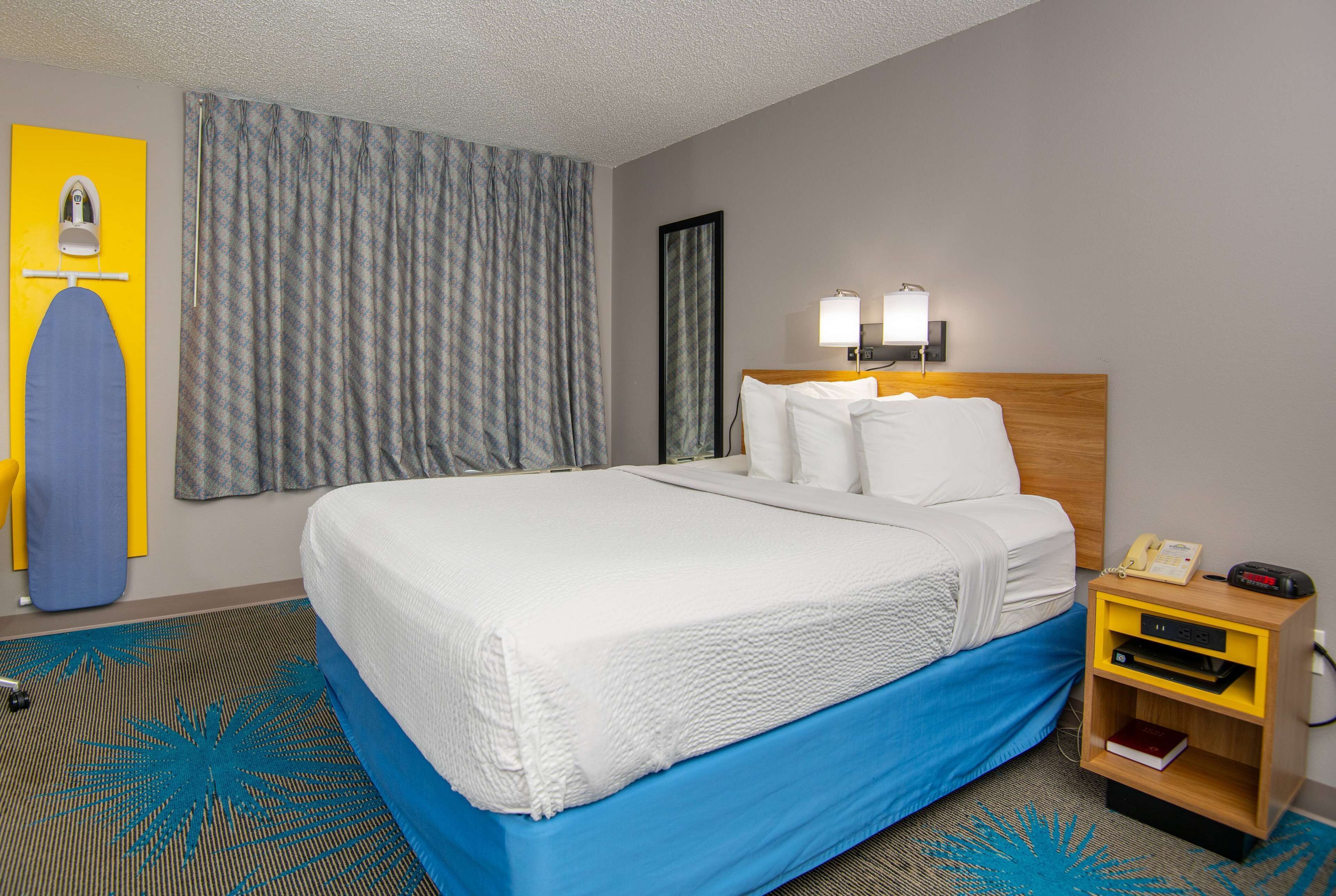 A hotel room with a bed, a nightstand, a lamp, and a mirror.