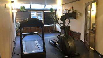 A gym with a treadmill and an elliptical machine, a window with blinds, and a door leading to another room.