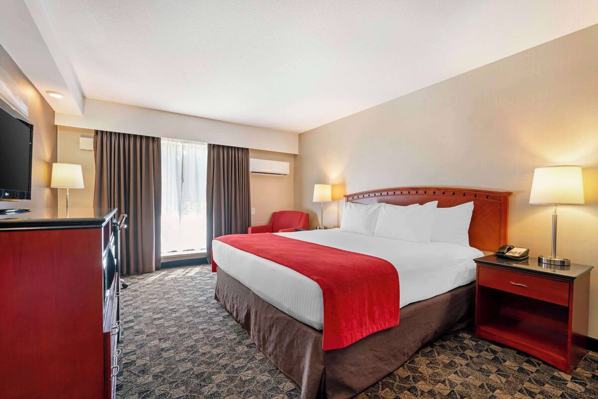 A hotel room with a large bed, a desk with a TV, a chair, and two bedside lamps.