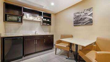 A compact kitchen with a built-in microwave, stove, and dishwasher. There is a dining table with two chairs and a wall-mounted artwork.