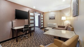 Habitación de hotel con escritorio, silla, sofá, televisor y alfombra estampada.