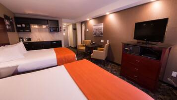 A hotel room with two beds, a kitchenette, a TV, and a desk with chairs.