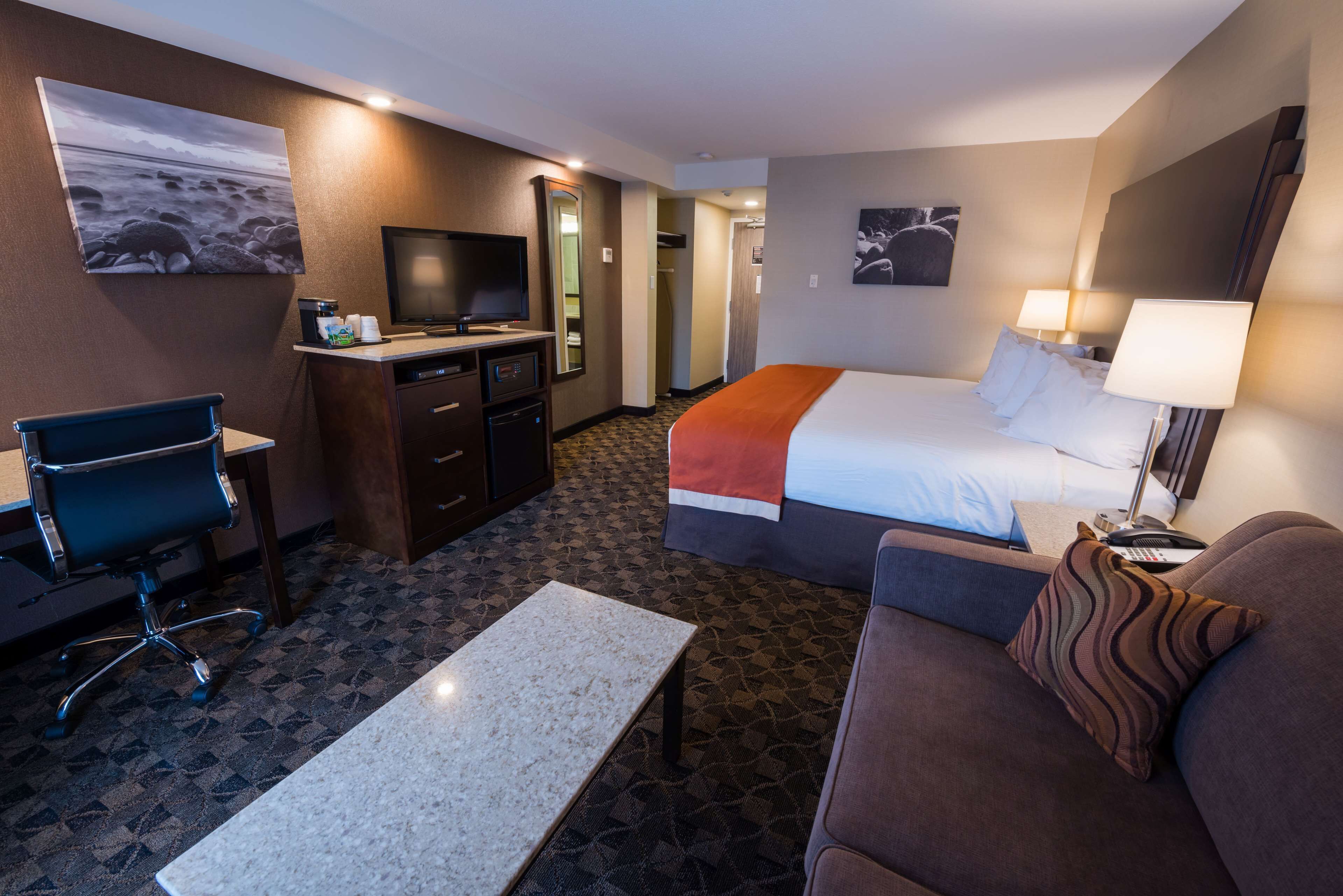 A hotel room with a bed, a desk, a chair, a TV, and a coffee machine.
