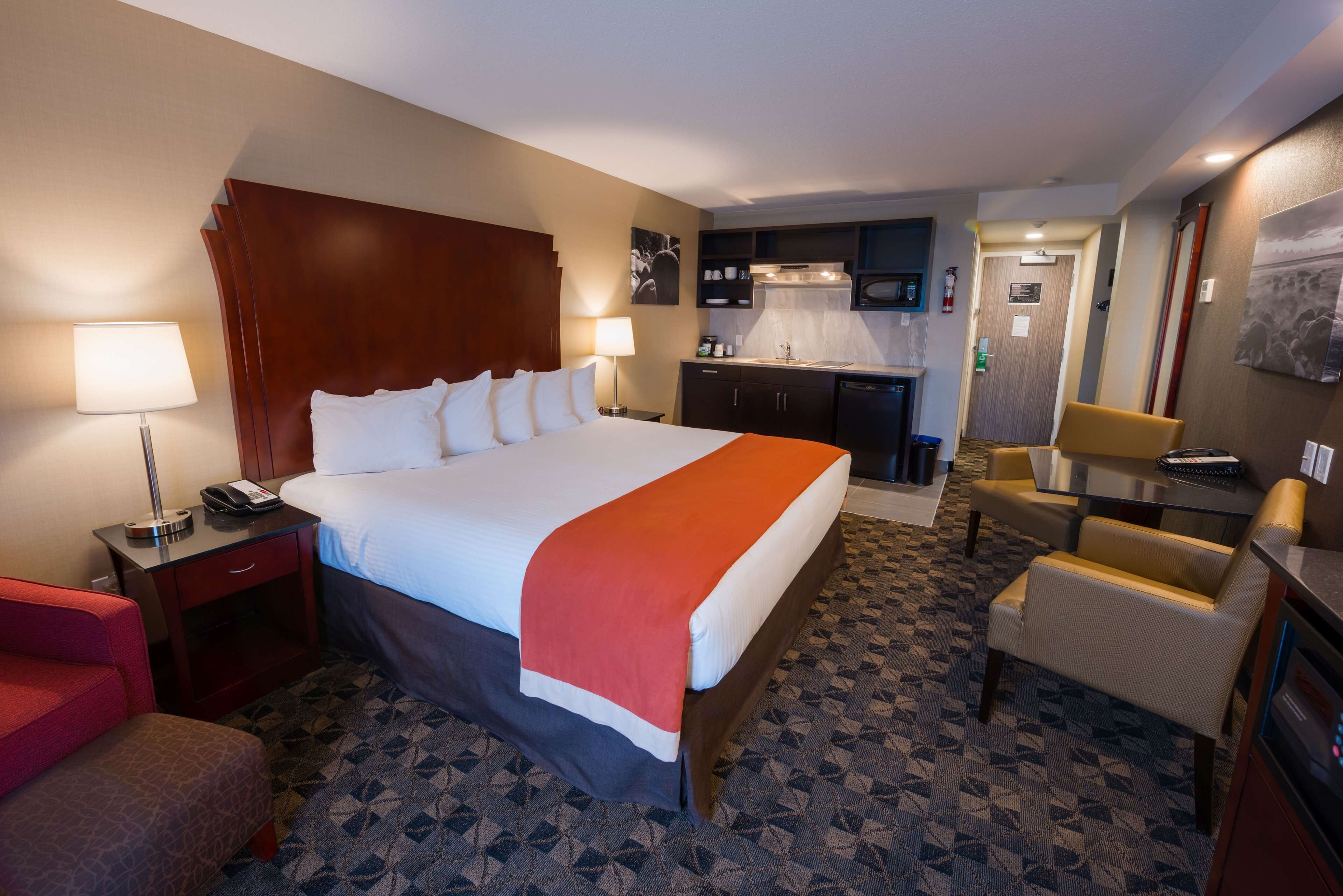 A hotel room with a large bed, a desk, a chair, a small kitchenette, and a bathroom.