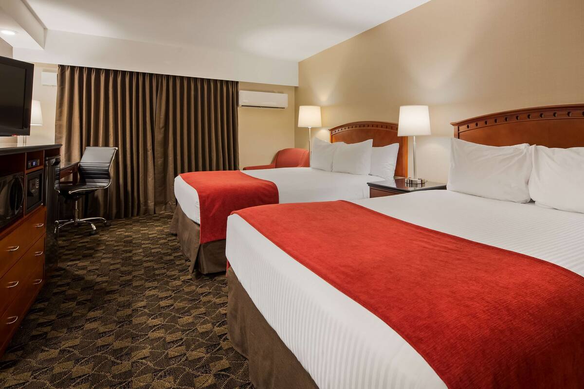 A hotel room with two beds, a desk with a chair, a television, and a window with curtains.
