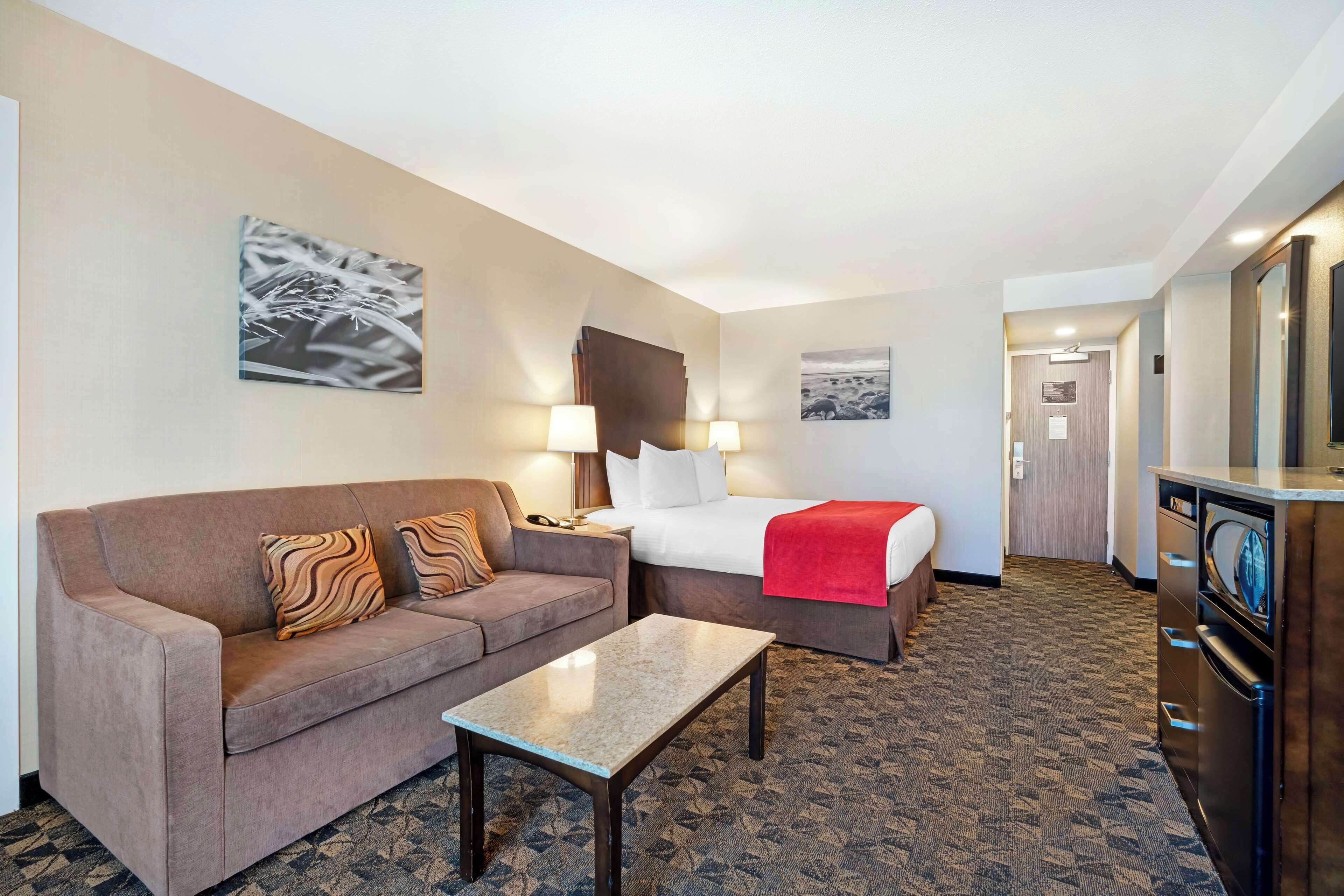 Quarto de hotel com sofá, cama, uma mesa pequena e cozinha compacta.