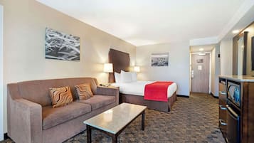 Quarto de hotel com sofá, cama, uma mesa pequena e cozinha compacta.
