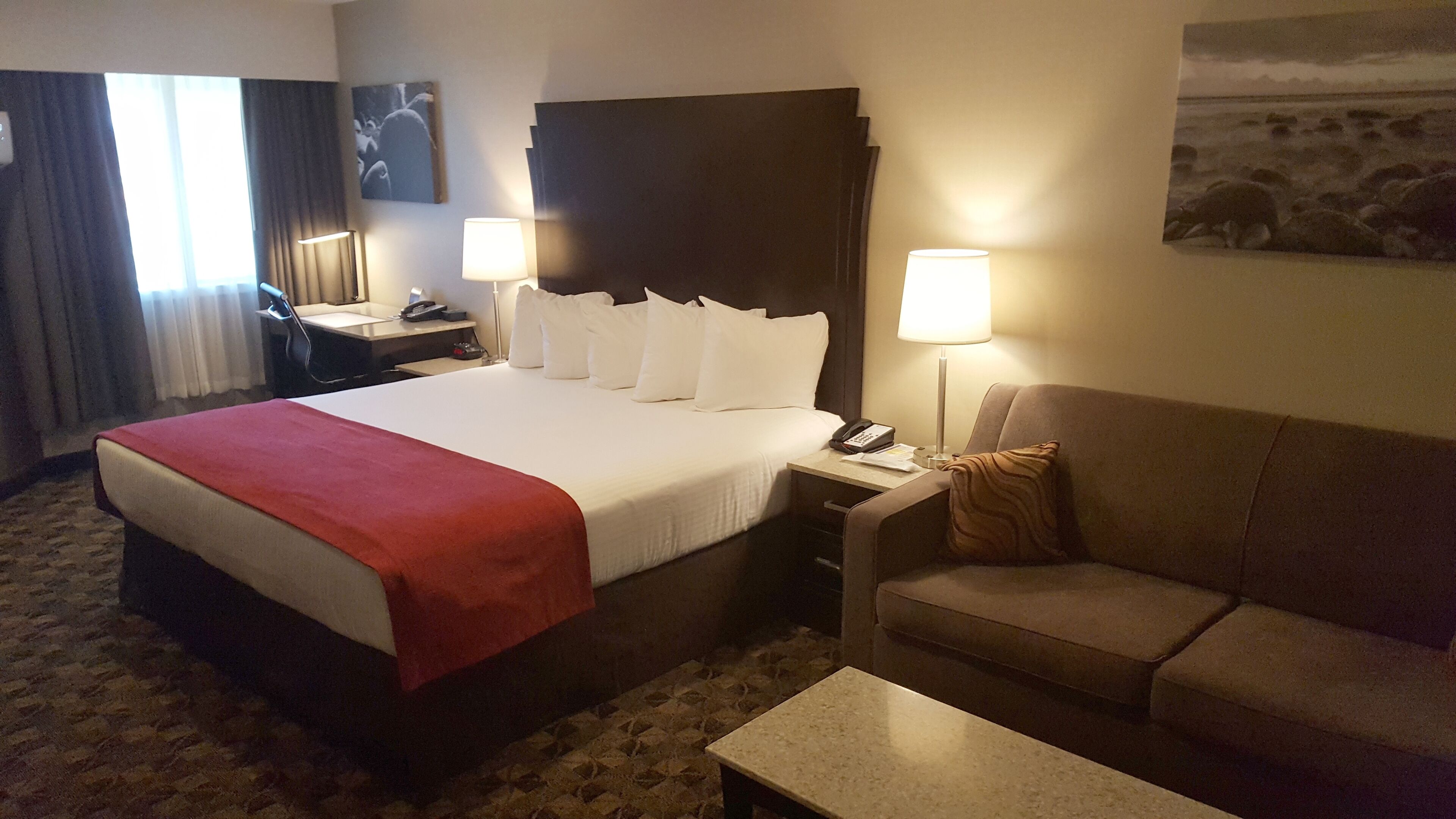 Una habitación de hotel con una cama, un escritorio con lámpara, una silla y un sofá.