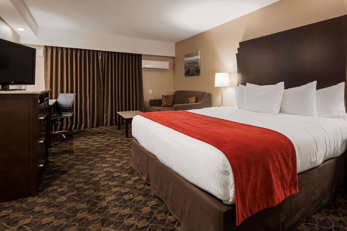 A hotel room with a large bed, a desk with a chair, a television, and a lamp.