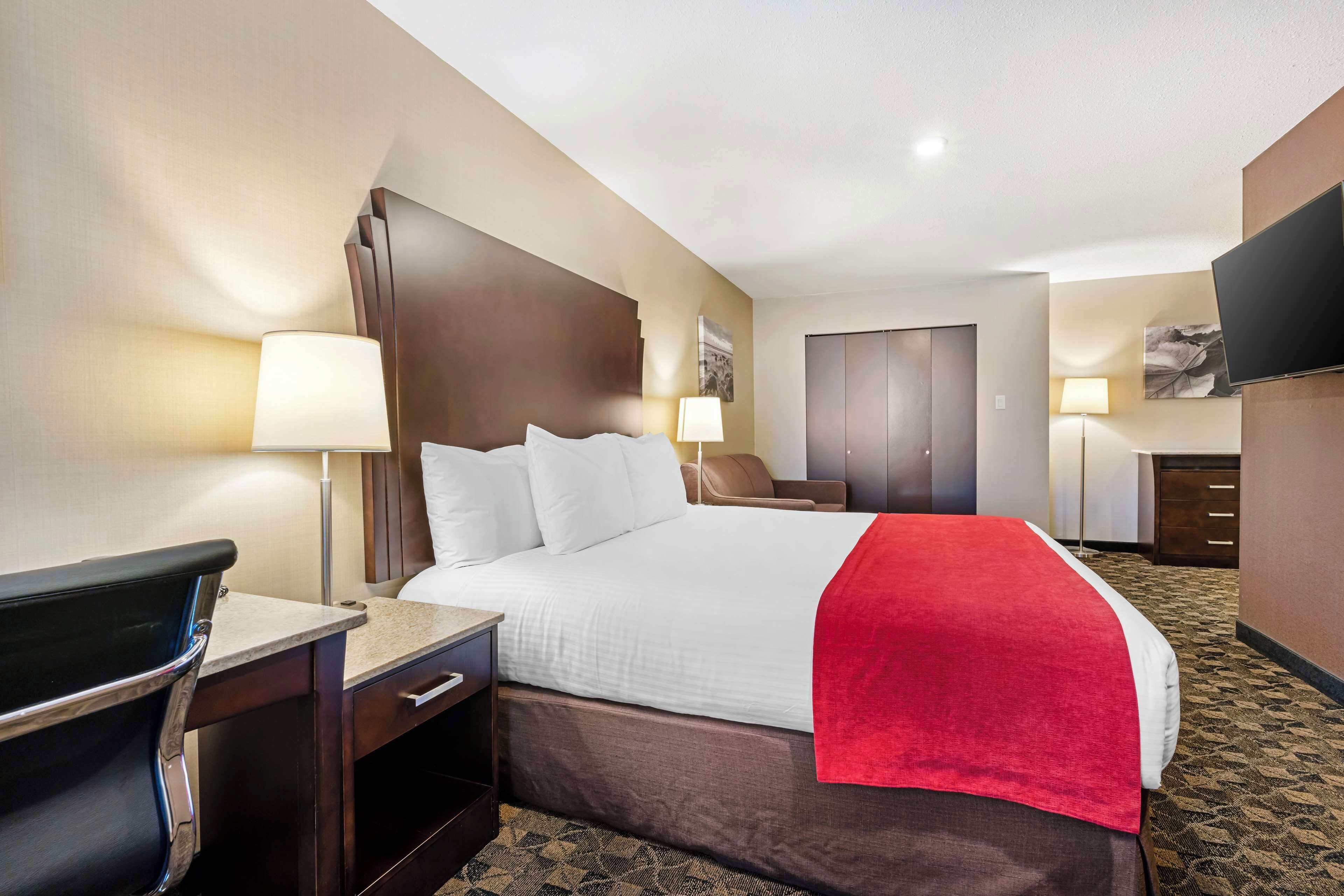 A hotel room with a bed, bedside tables, lamps, a TV, and a desk.