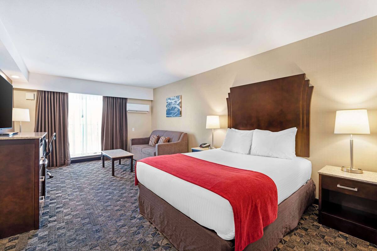 A hotel room with a large bed, a desk, a chair, a TV, and a window with curtains.