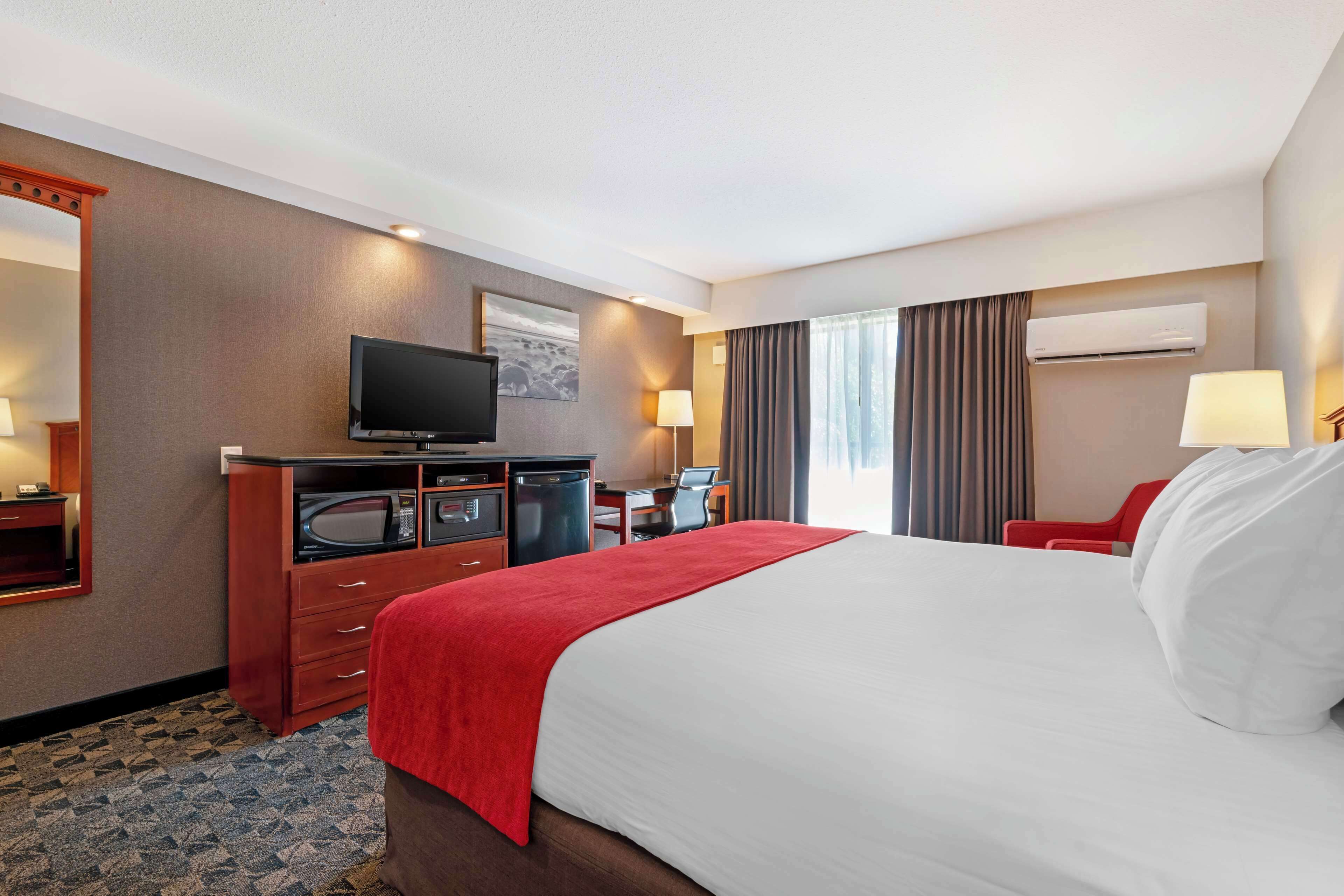 Une chambre d’hôtel avec un grand lit, un bureau avec un ordinateur, une télévision et un fauteuil rouge.
