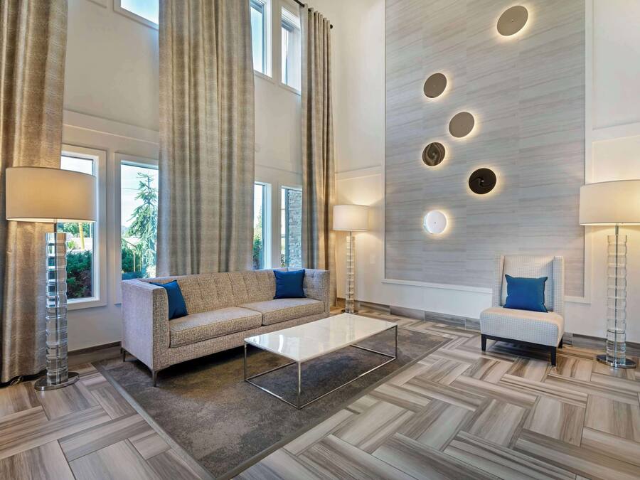 A spacious living room with a sofa, armchair, and coffee table, large windows, and a modern wall design.