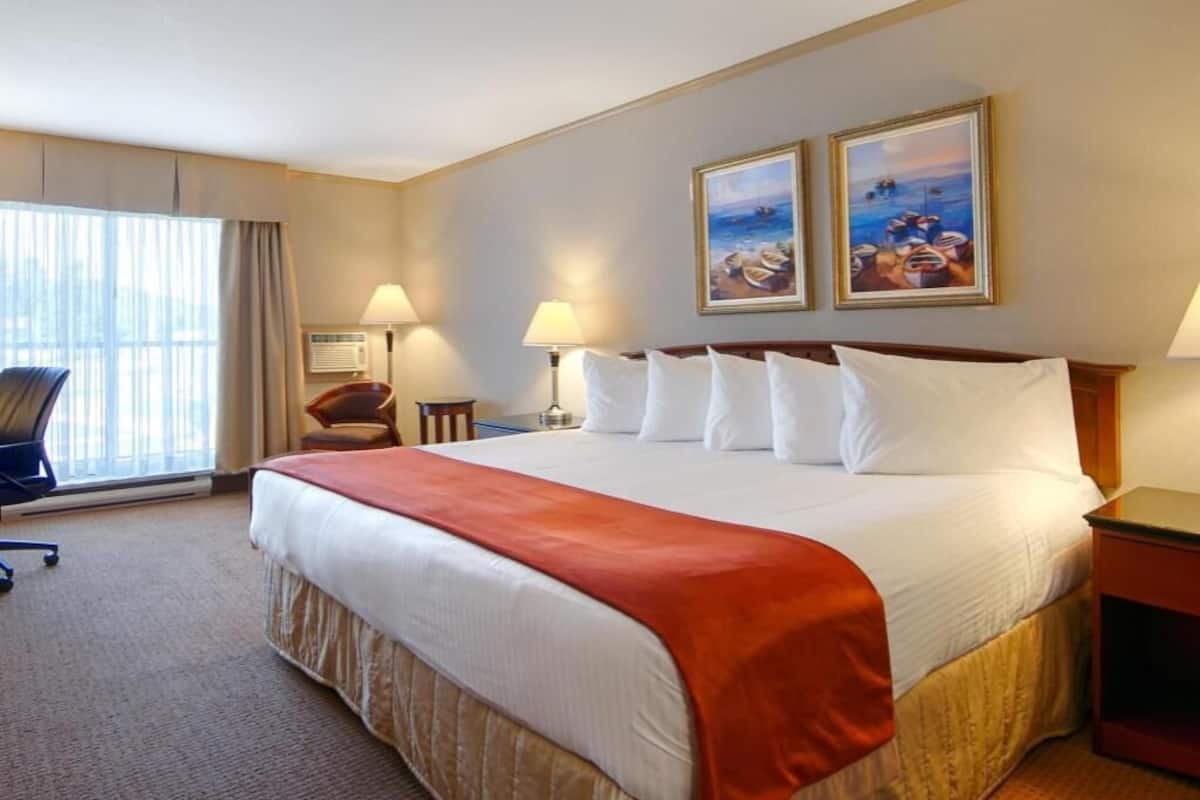 A hotel room with a large bed, two bedside lamps, a chair, a desk, and a window with curtains.