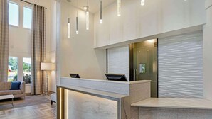 Un área de recepción moderna con mostrador de mármol, iluminación colgante y vistas al exterior.