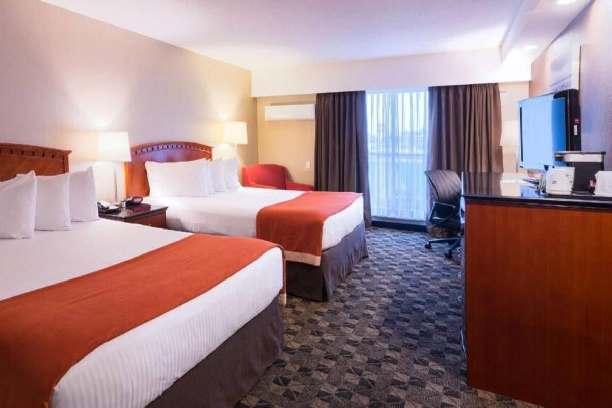 A hotel room with two beds, a desk, a chair, a television, and a window with curtains.