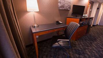 Una camera d'albergo con una scrivania, una sedia, una lampada, televisione e un piccolo armadietto.