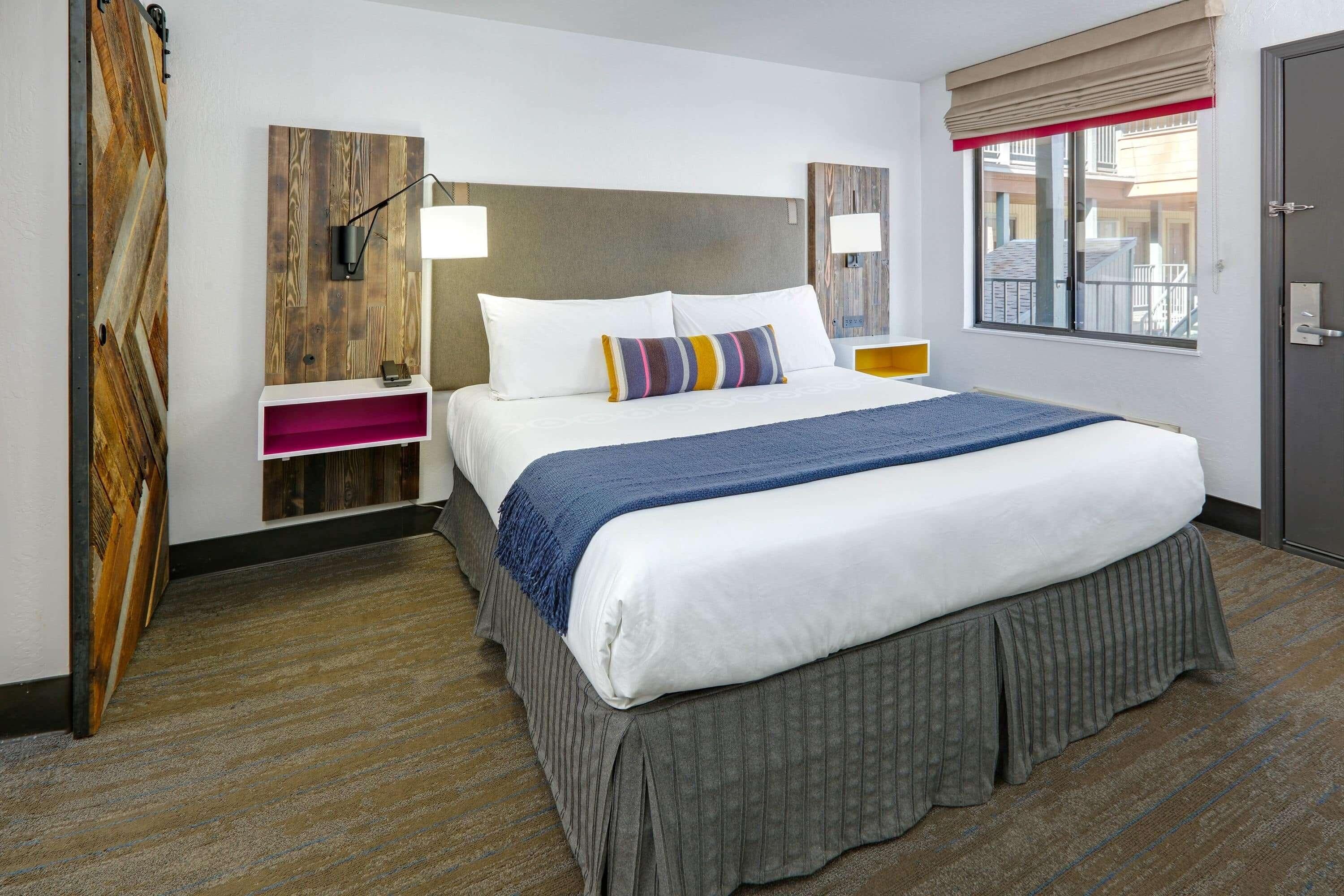 A hotel room with a bed, bedside tables, a window, and a door.