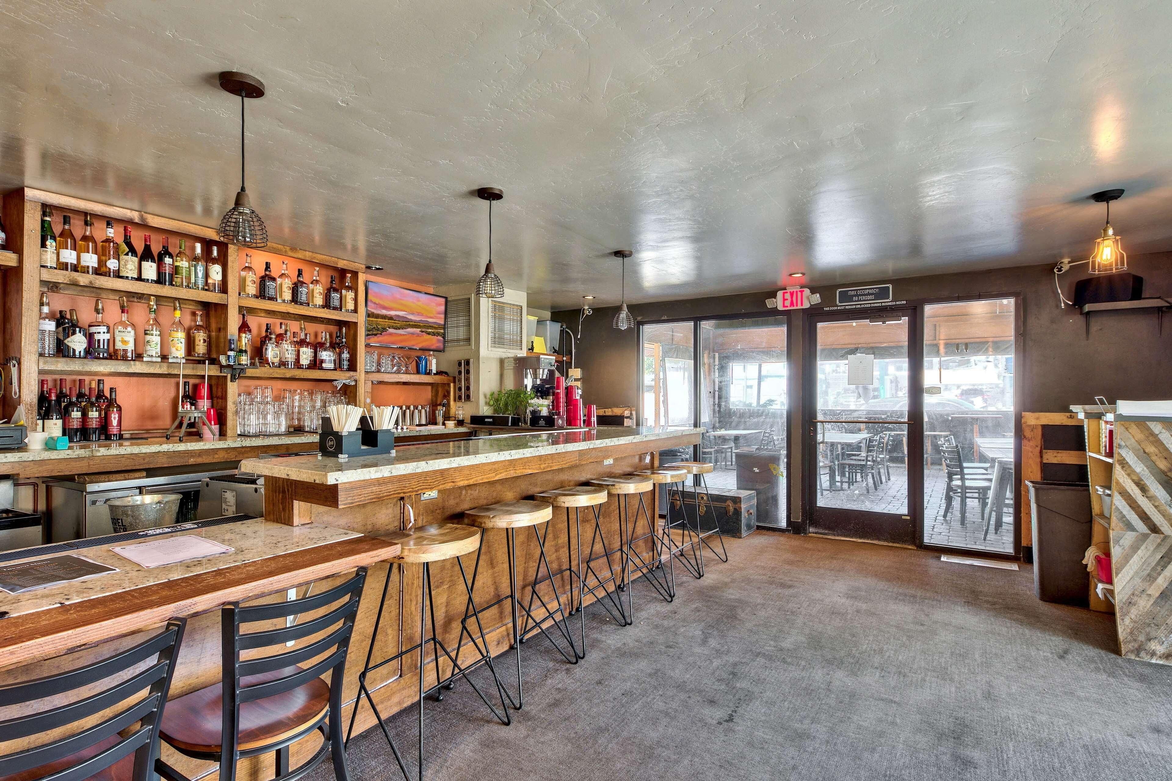 A bar area with a wooden counter, stools, and a variety of bottles.