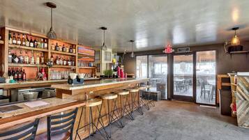 A bar area with a wooden counter, stools, and a variety of bottles.
