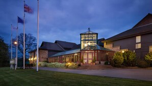 A hotel with a prominent tower, a well-lit entrance, and multiple flags. - Mercure Hatfield Oak (Hatfield)