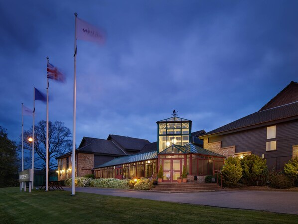 A hotel with a prominent tower, a well-lit entrance, and multiple flags. - Mercure Hatfield Oak (Hatfield)