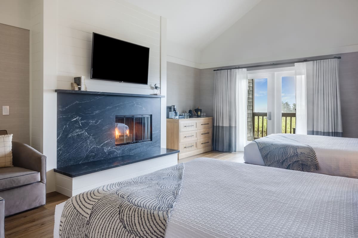A modern hotel room with a fireplace, a flat-screen TV, a balcony with curtains, and two beds.