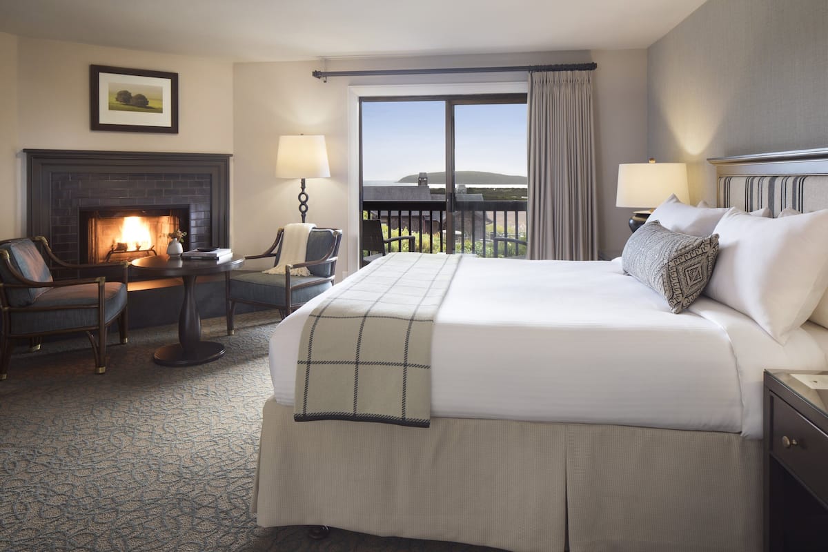 A hotel room with a large bed, a fireplace, a desk with a chair, and a view of the outdoors.
