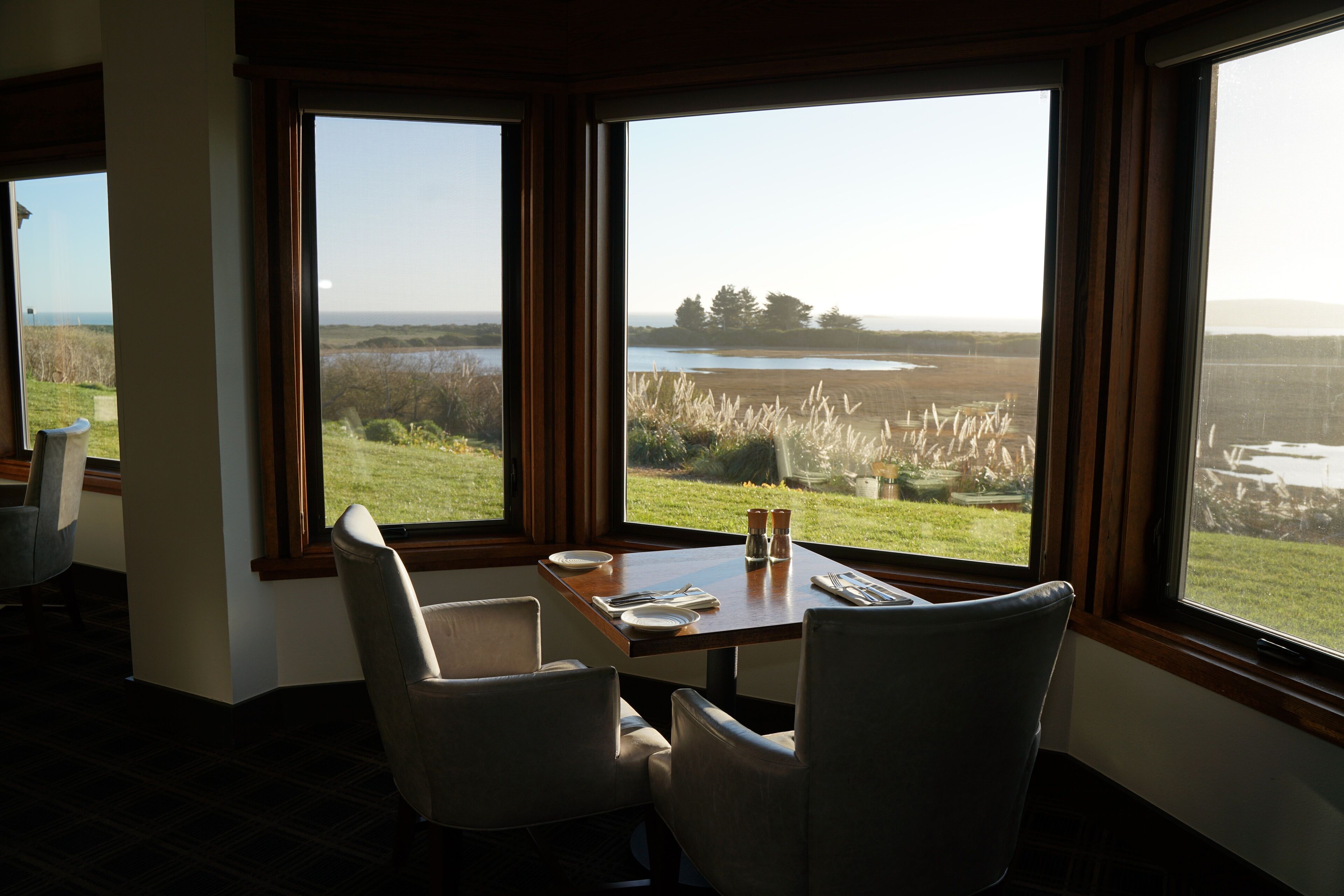 A dining area with a table set for two, large windows offering a view of a lake and surrounding landscape.