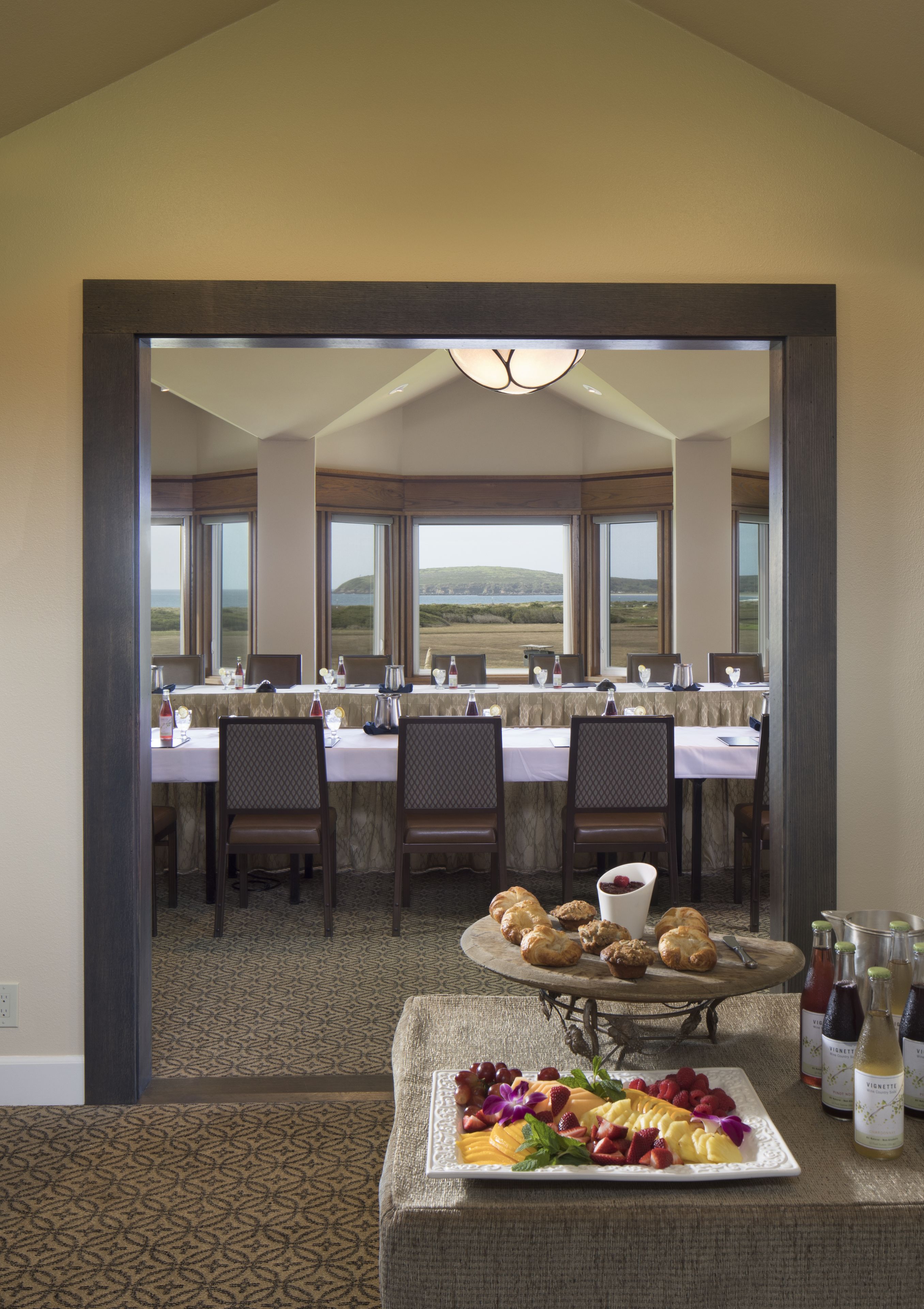 Uma área de refeições com uma mesa posta para uma refeição, um buffet com doces e frutas, e garrafas de vinho.