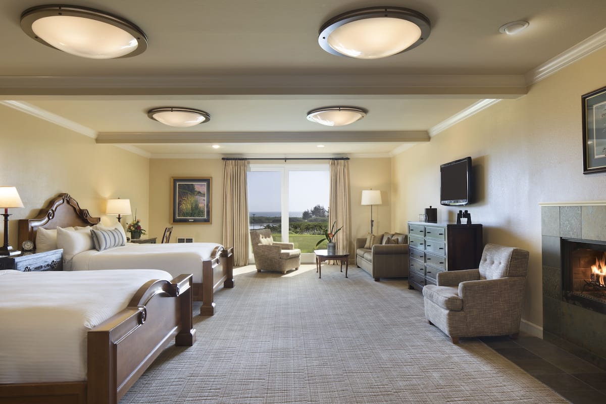 A hotel room with two beds, a fireplace, a television, and a view of the outdoors.
