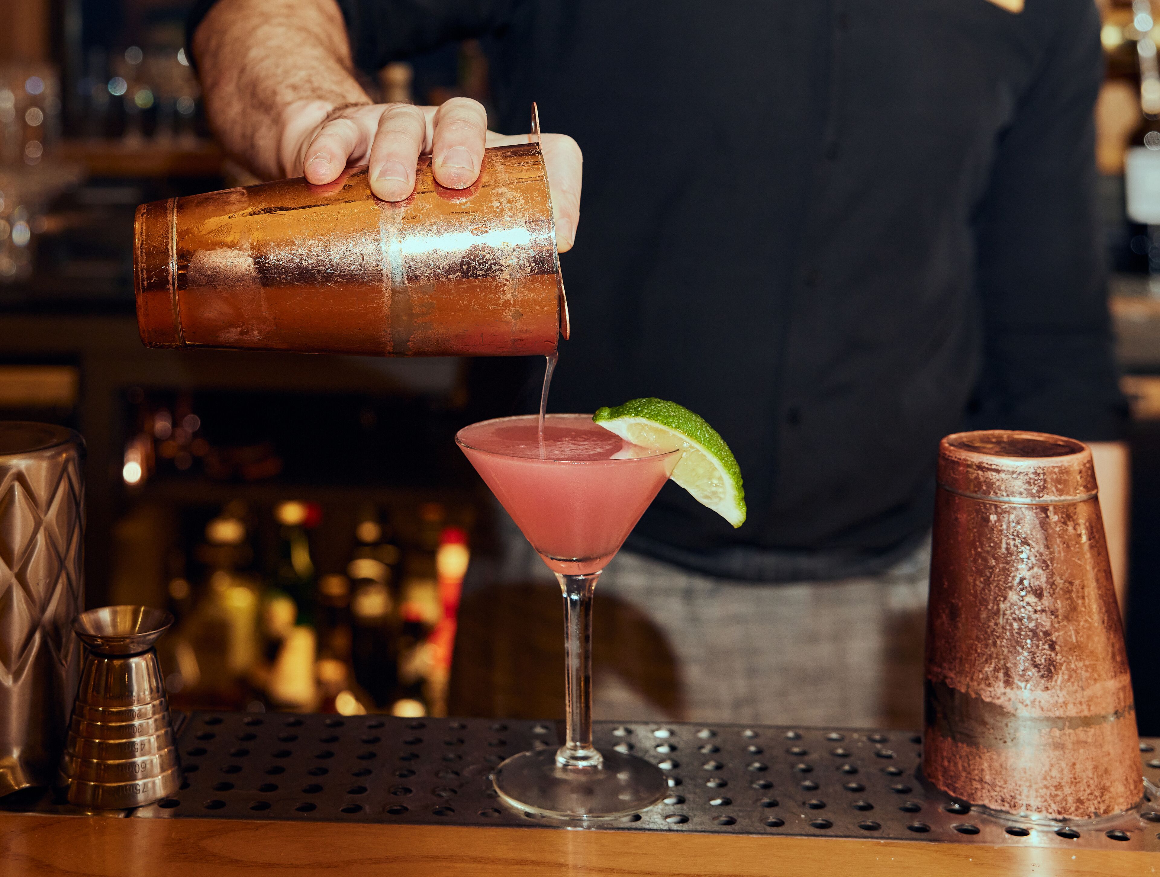 A bartender pouring a drink into a martini glass with a lime garnish.