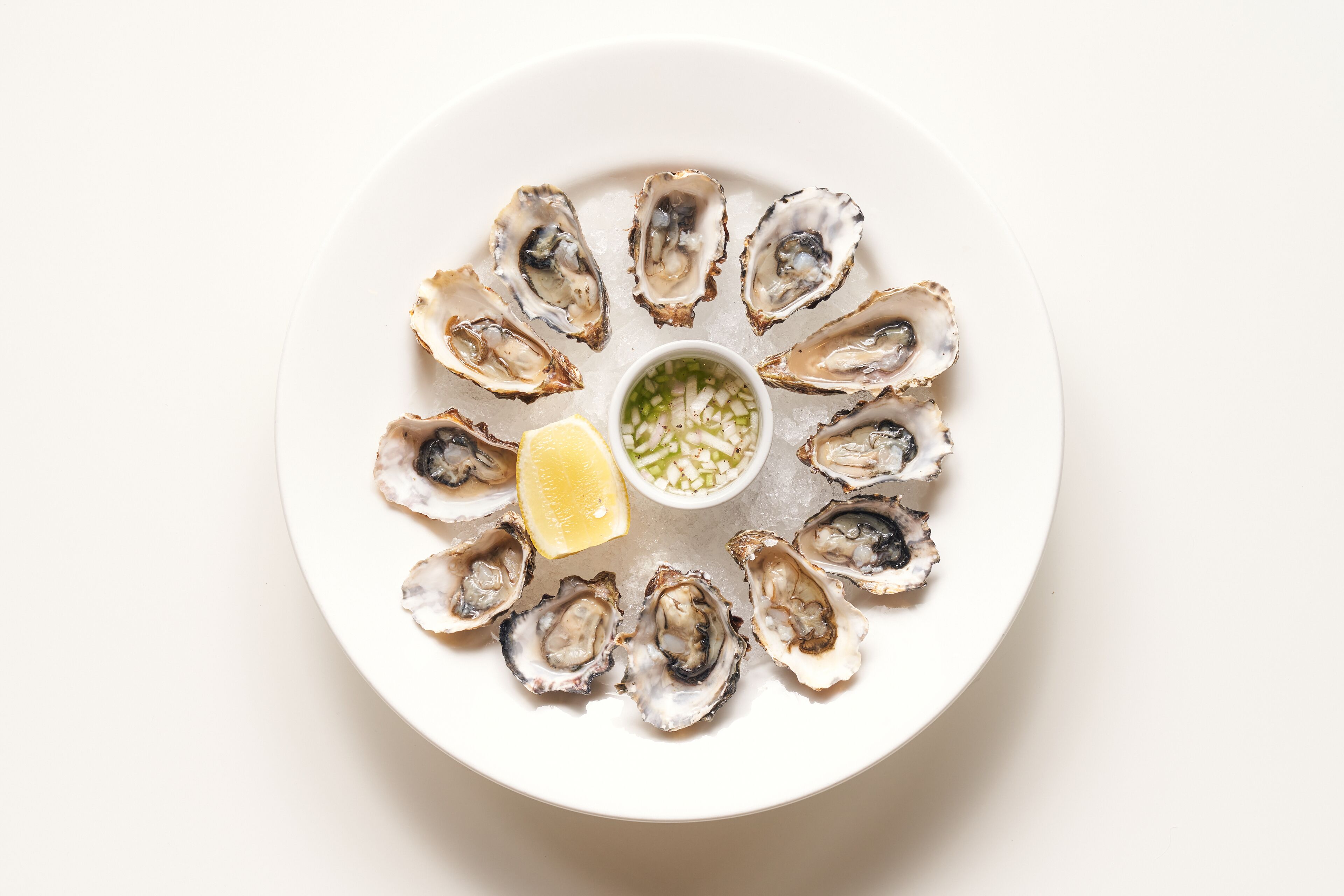 A plate of oysters with a lemon wedge and a small bowl of sauce.