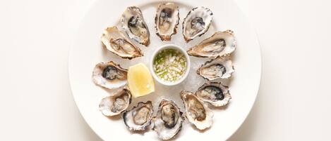 A plate of oysters with a lemon wedge and a small bowl of sauce.