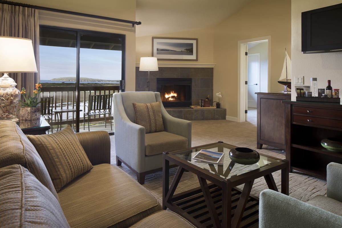 A living room with a fireplace, a sofa, a chair, a coffee table, and a view of the outdoors.