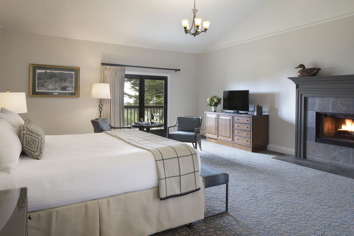 A hotel room with a large bed, a television, a fireplace, and a view of the outdoors through a sliding door.