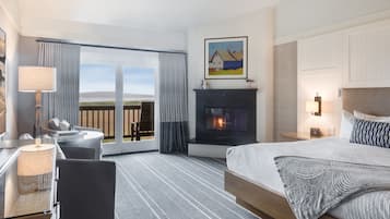A hotel room with a bed, a desk, a chair, a fireplace, and a large window with curtains.