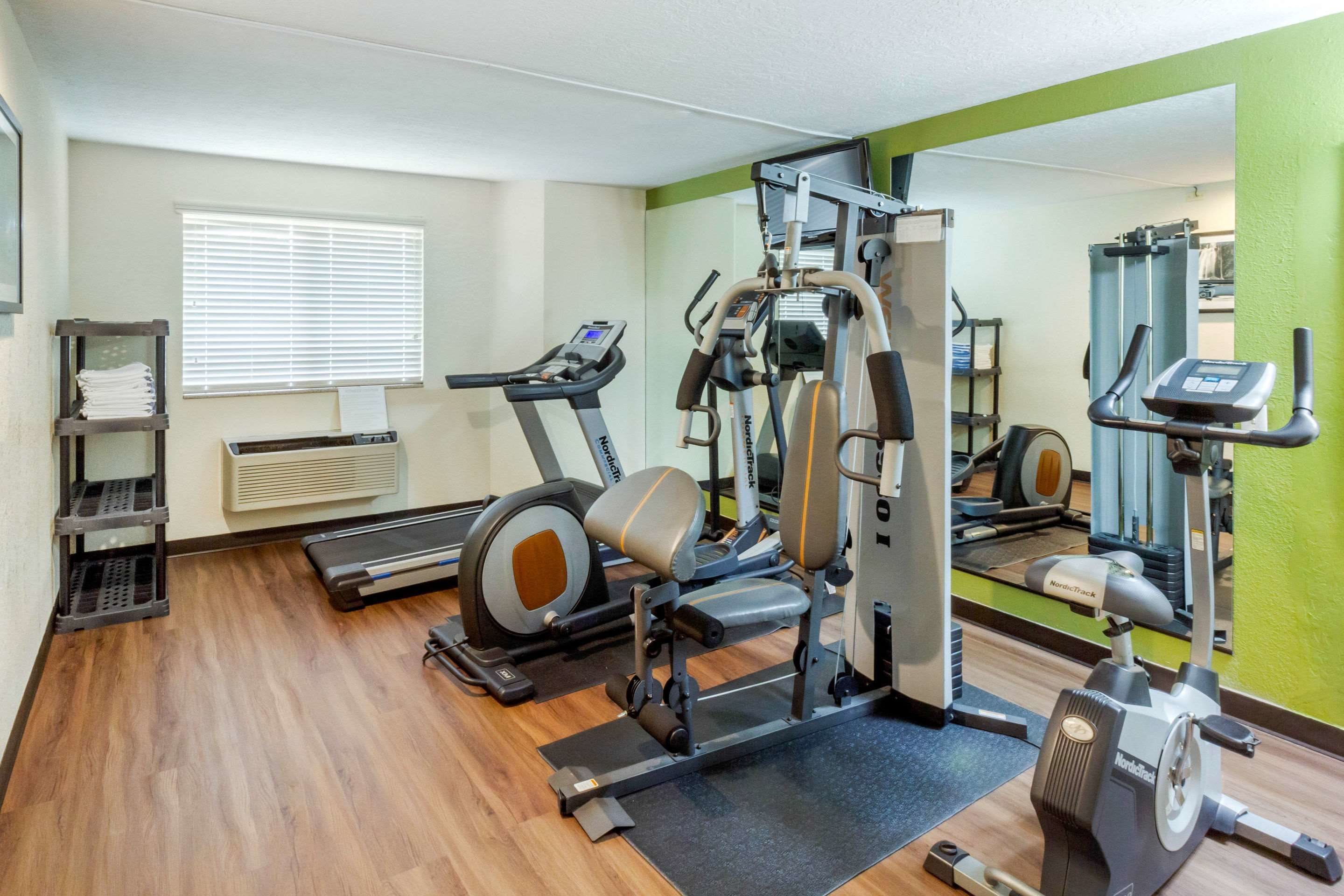 A gym with cardio machines, weight training equipment, and a mirrored wall.