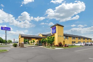 Un hotel Sleep Inn con fachada amarilla, un acceso cubierto y un estacionamiento con varios coches.