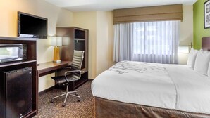 A hotel room with a bed, a desk with a chair, a television, a microwave, and a window with curtains.